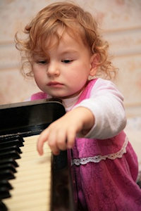 Little girl tentatively touching a piano keyboard